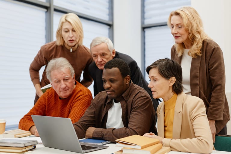 A diverse group of individuals gathered around a laptop