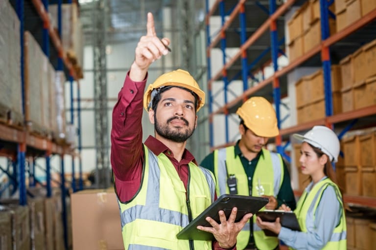 A man wearing a hard hat and safety vest is holding a tablet