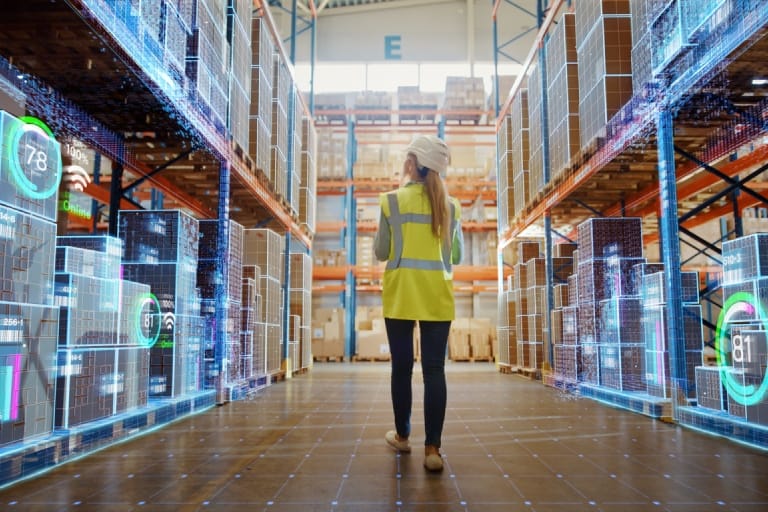 A woman in a yellow vest walks through a spacious warehouse