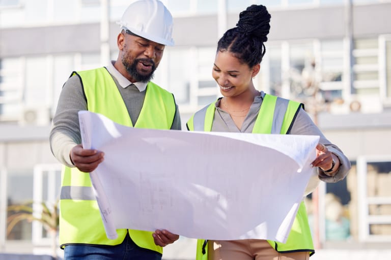 Two workers in hard hats analyze a blueprint